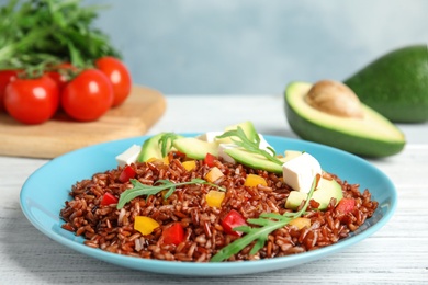 Photo of Plate with delicious cooked brown rice on white wooden table