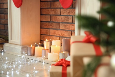 Photo of Christmas lights near decorative fireplace with candles indoors