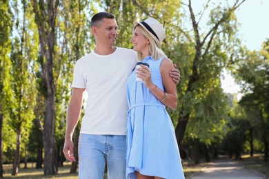 Happy couple with drink walking along park on summer day