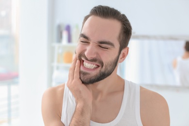 Photo of Young man suffering from toothache indoors