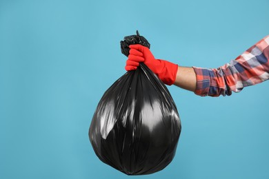 Photo of Man holding full garbage bag on light blue background, closeup