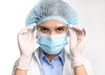 Photo of Doctor with medical gloves, mask, cap and protective goggles on white background