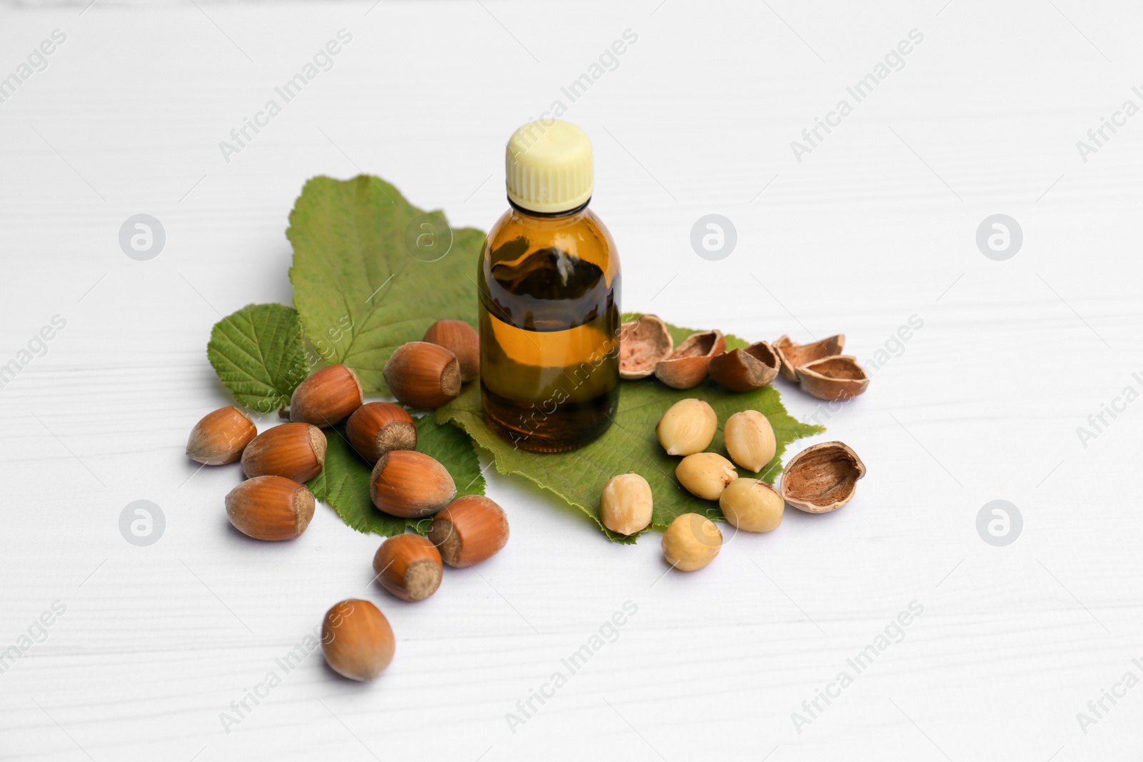 Photo of Bottle of hazelnut essential oil and nuts on white wooden table
