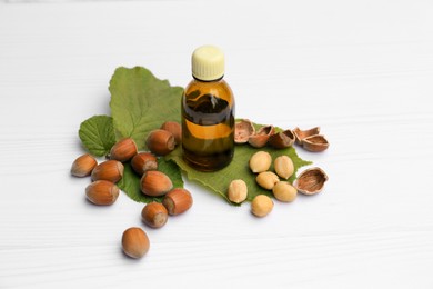 Bottle of hazelnut essential oil and nuts on white wooden table