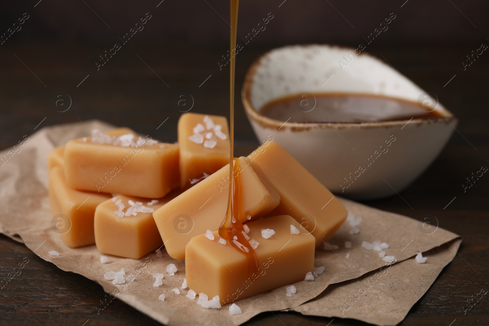 Photo of Pouring caramel on candies with sea salt at table, closeup