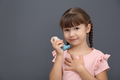 Photo of Little girl with asthma inhaler on grey background