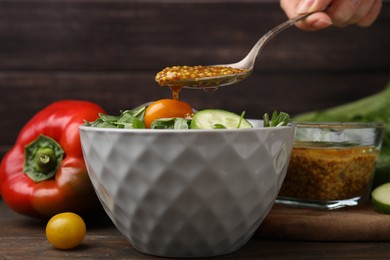 Photo of Woman pouring tasty vinegar based sauce (Vinaigrette) from spoon into bowl with salad at wooden table, closeup