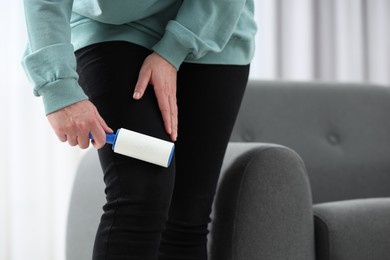 Photo of Woman with lint roller removing pet hair from black trousers indoors, closeup