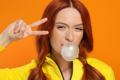 Photo of Beautiful woman in sunglasses blowing bubble gum and gesturing on orange background