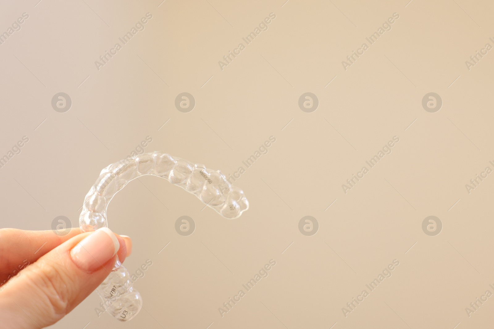 Photo of Woman with transparent dental aligner on beige background, closeup. Space for text