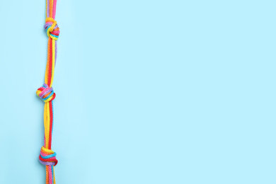 Photo of Top view of colorful ropes tied together on light blue background, space for text. Unity concept