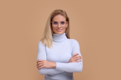 Photo of Portrait of smiling middle aged woman in glasses with crossed arms on beige background
