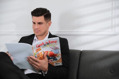 Photo of Man reading new magazine on sofa indoors