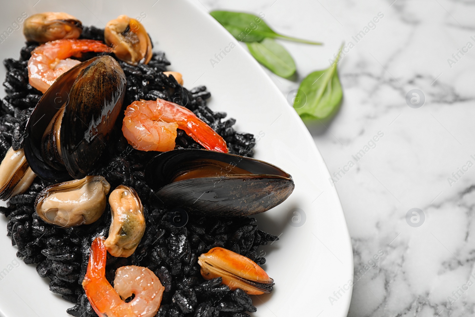 Photo of Delicious black risotto with seafood on white marble table, closeup