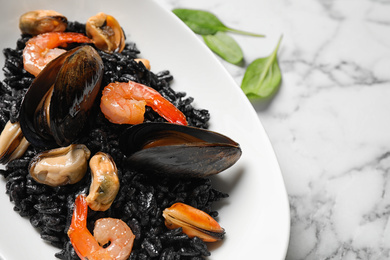 Delicious black risotto with seafood on white marble table, closeup