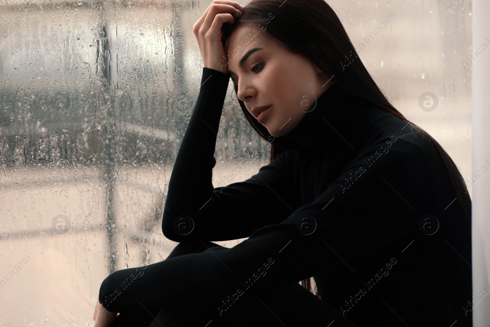 Photo of Depressed woman near window on rainy day