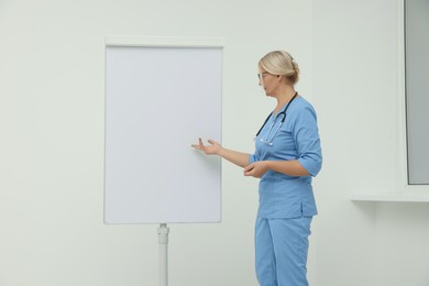 Photo of Professional doctor explaining something near flipchart indoors