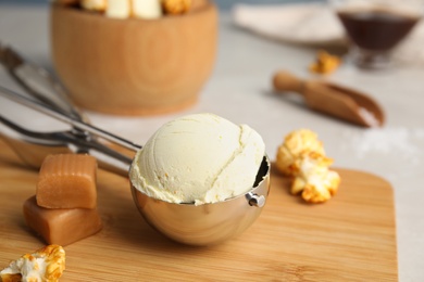 Photo of Delicious ice cream in scoop, caramel and popcorn on wooden board