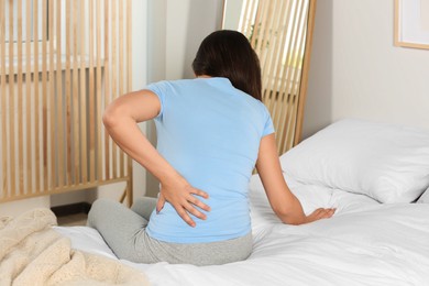 Photo of Young woman suffering from back pain while sitting on bed at home. Symptom of scoliosis