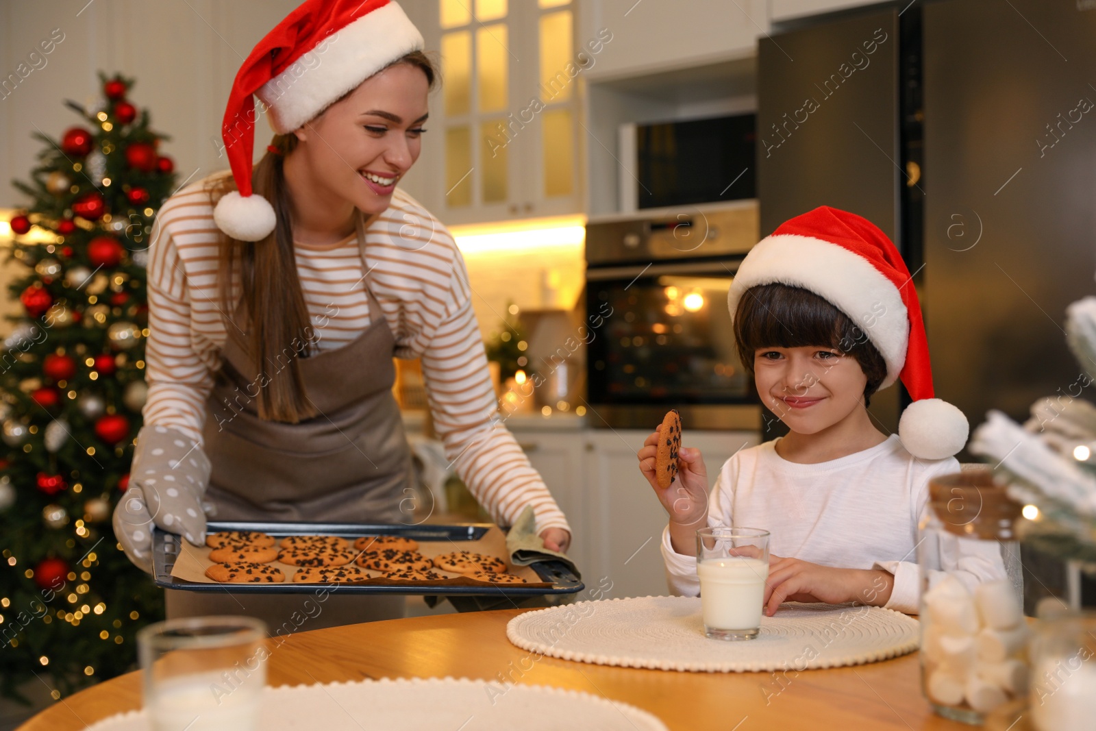 Photo of Mother giving her cute little son freshly baked Christmas cookie in kitchen