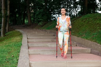 Photo of Young woman practicing Nordic walking with poles on steps outdoors. Space for text