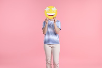 Photo of Woman holding emoticon with stars instead of eyes on pink background