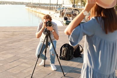 Photo of Male photographer taking photo of young woman with professional camera at pier