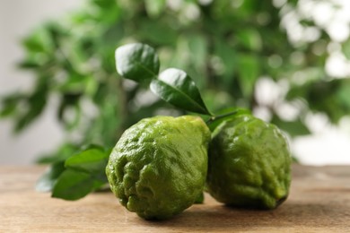 Fresh ripe bergamot fruits with green leaves on wooden table against blurred background