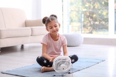Little girl relaxing in front of fan at home. Summer heat