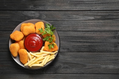 Photo of Tasty fried chicken nuggets with garnish on wooden table, top view. Space for text