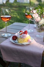 Photo of Vase with spring flowers, wine and cake on table served for romantic date in garden