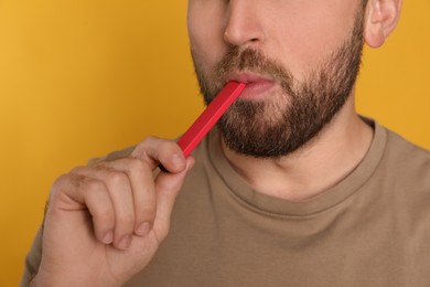 Man using electronic cigarette on yellow background, closeup