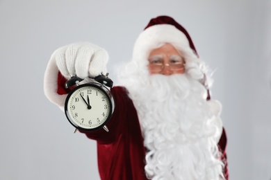 Santa Claus holding alarm clock on light grey background, focus on hand. Christmas countdown