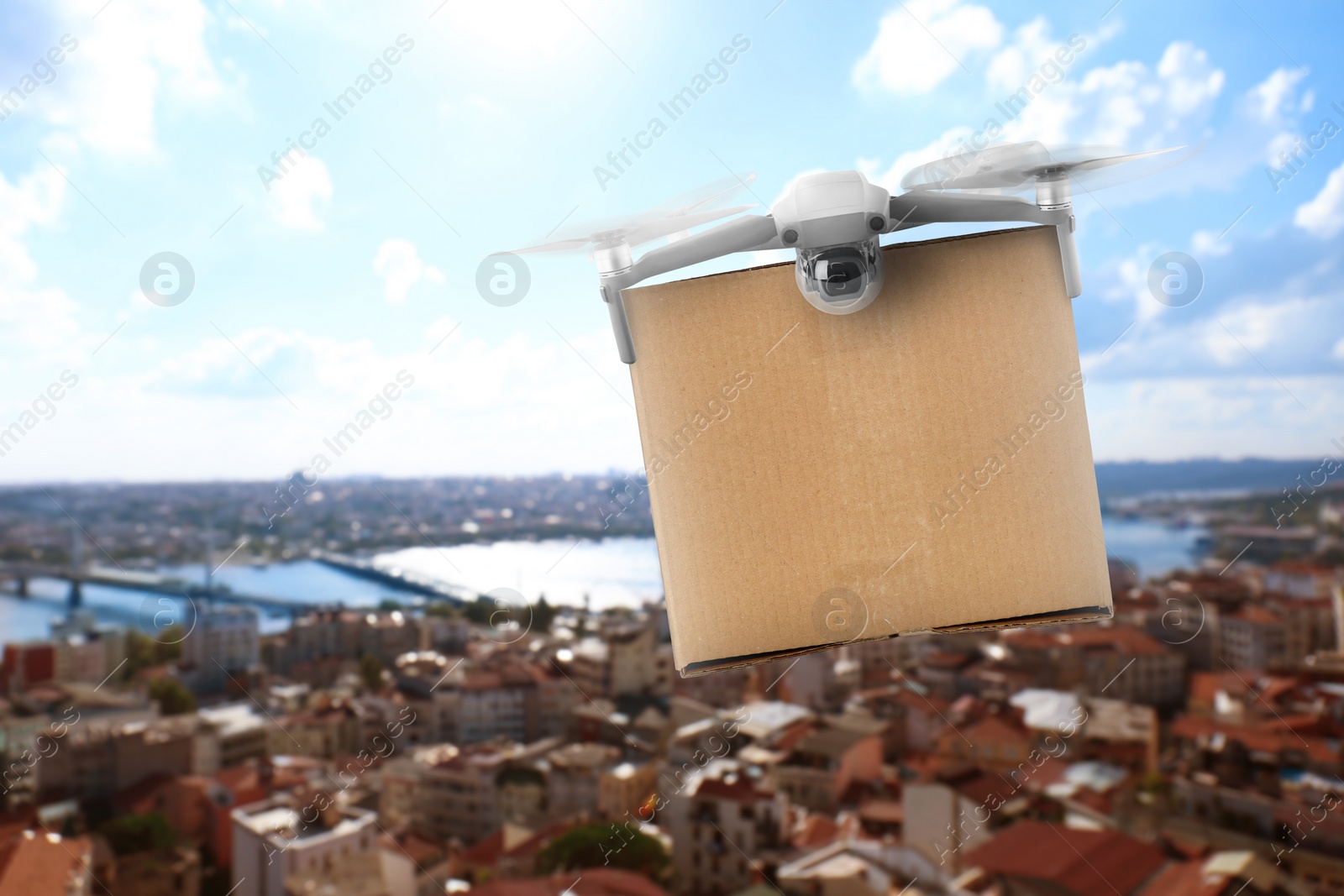 Image of Modern drone with carton box flying above city on sunny day. Delivery service 