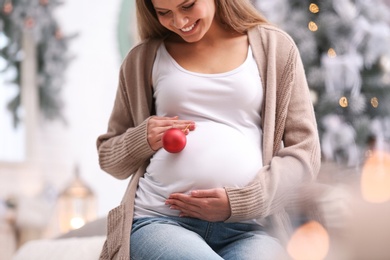 Photo of Young pregnant woman with Christmas decoration at home, closeup