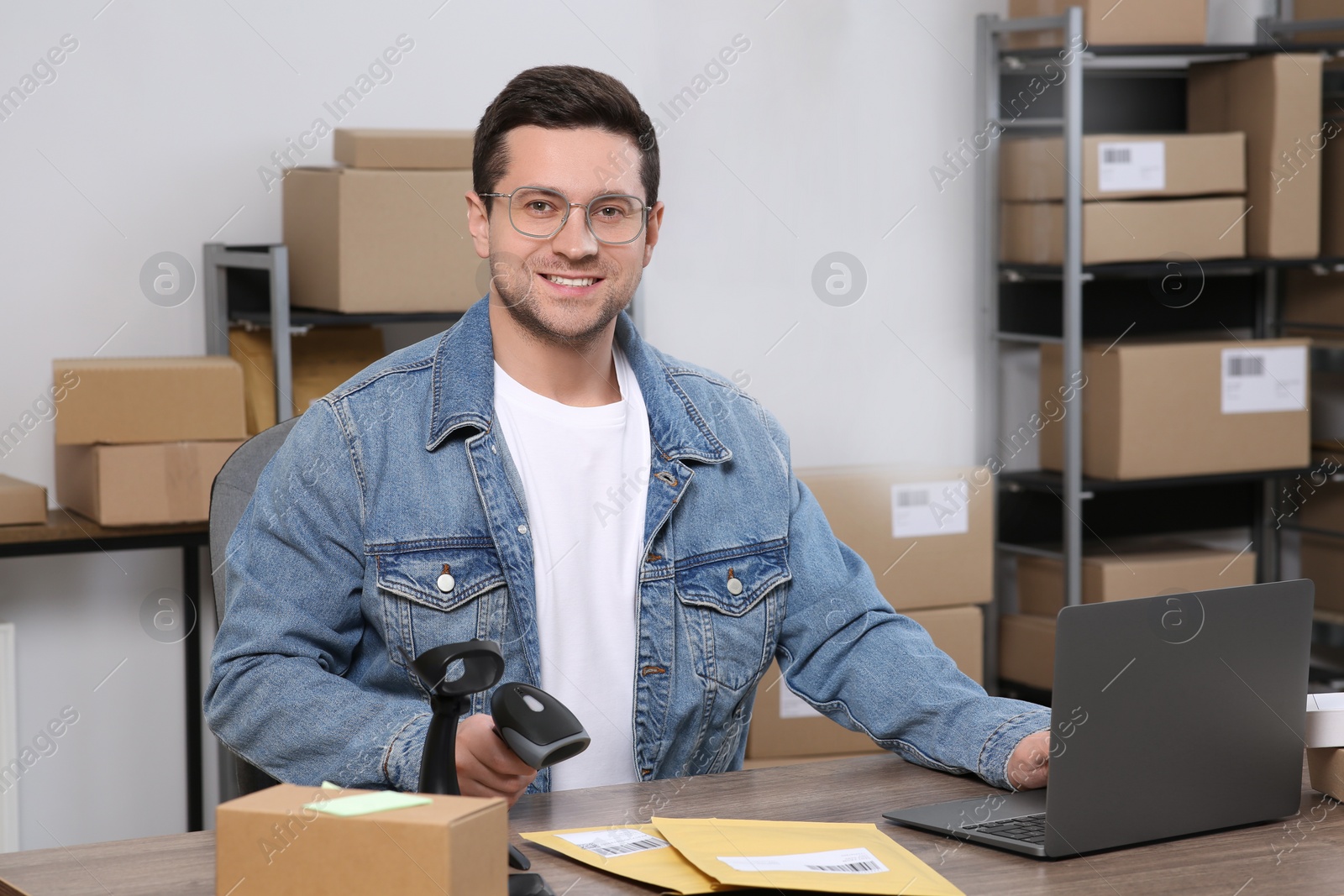 Photo of Seller with scanner, parcels and laptop at table in office. Online store