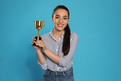 Portrait of happy young woman with gold trophy cup on blue background