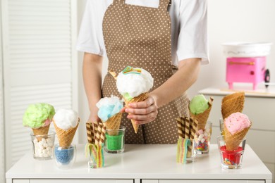 Photo of Woman holding waffle cone with cotton candy indoors, closeup