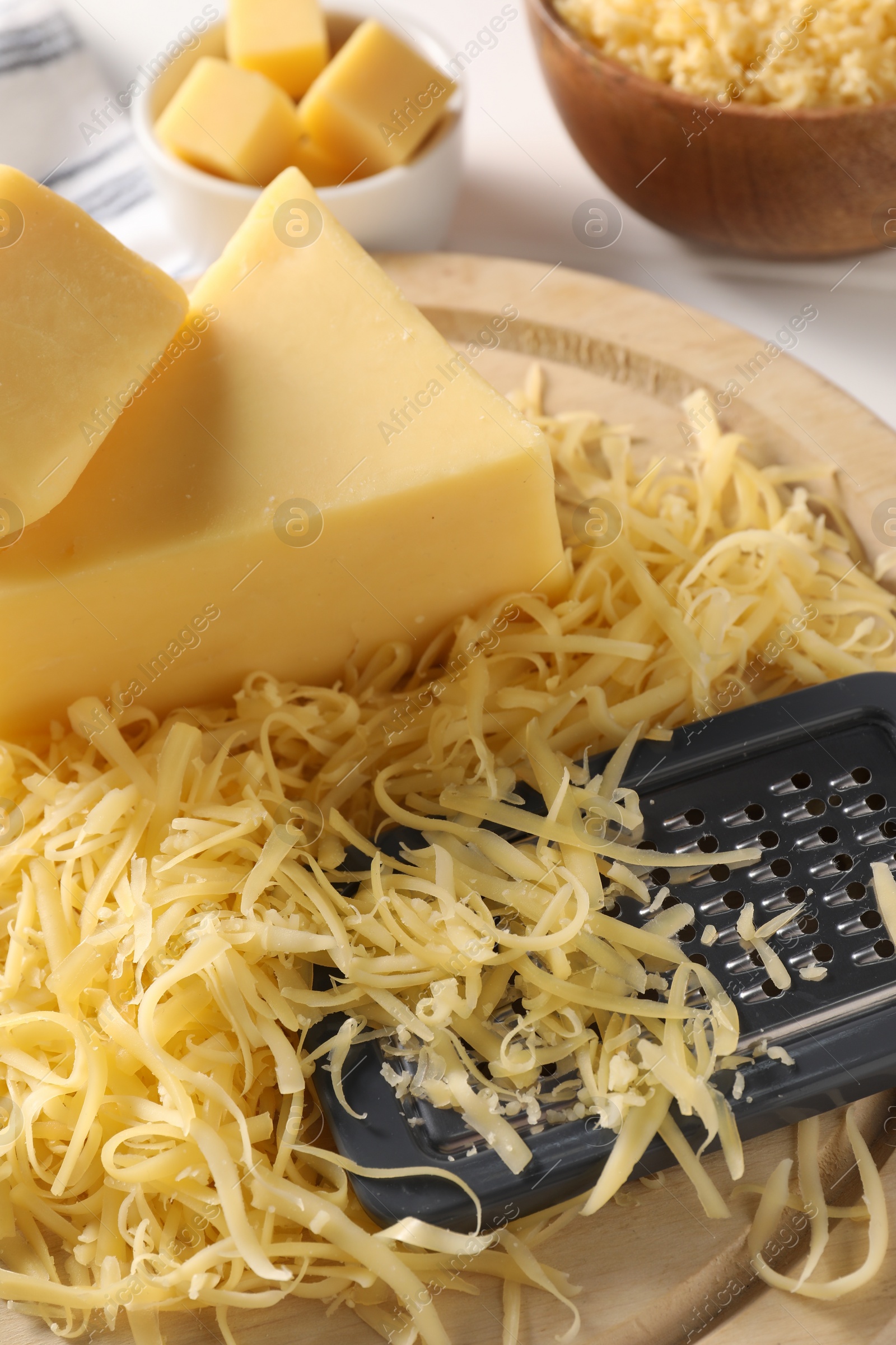 Photo of Grated, whole pieces of cheese and grater on table, closeup