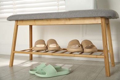 Stylish rubber slippers and storage bench with shoes in room