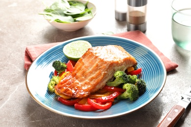 Plate with tasty cooked salmon and vegetables on table