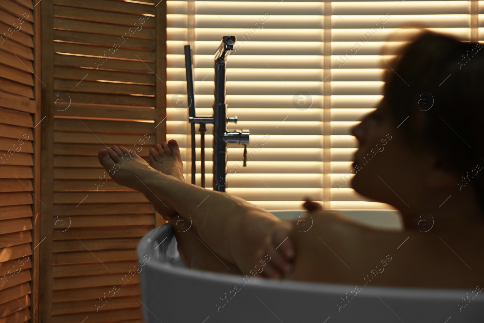Photo of Beautiful woman taking bath with foam in tub indoors, selective focus