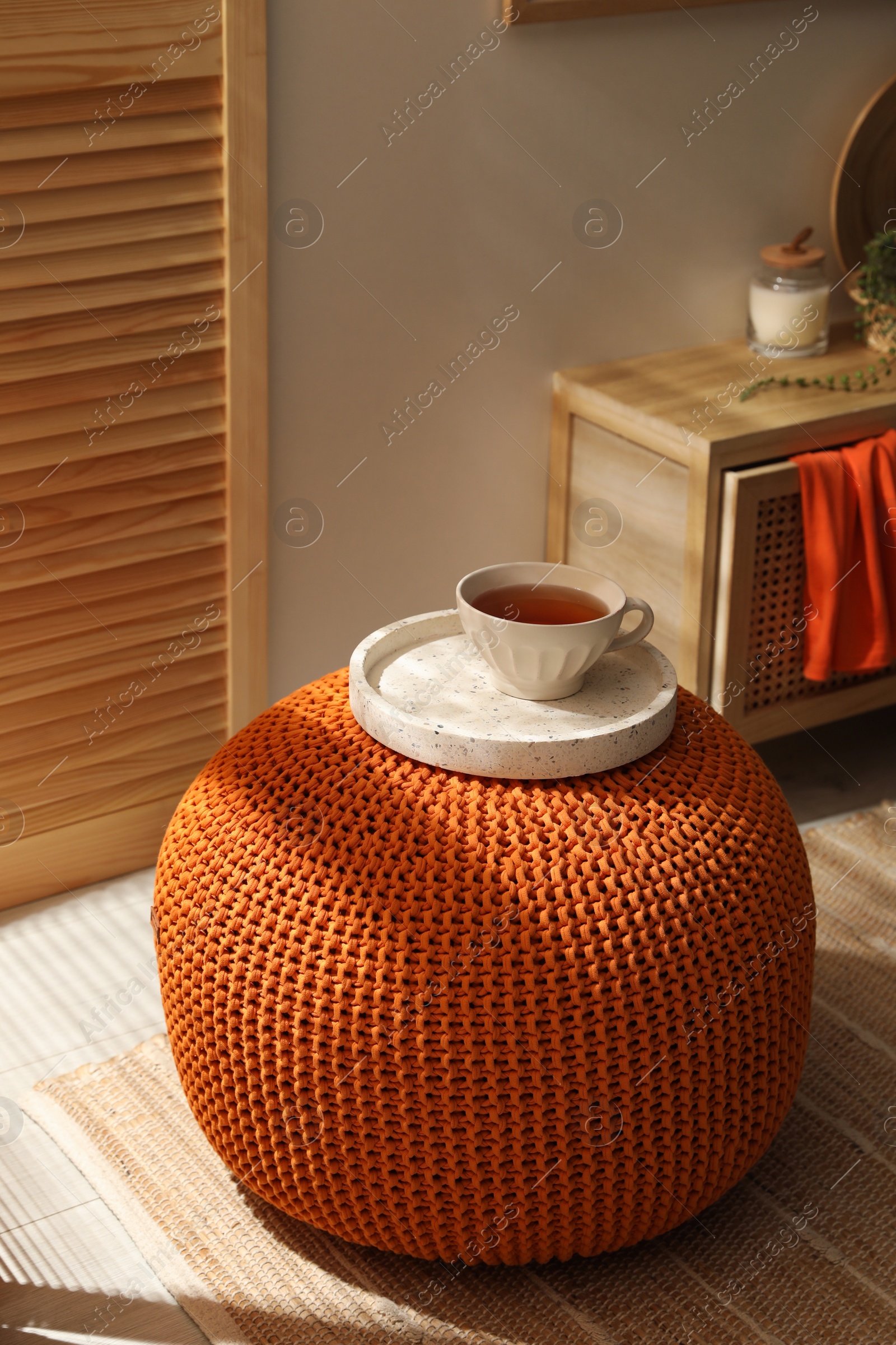 Photo of Tray with cup of tea on stylish comfortable pouf in room. Home design