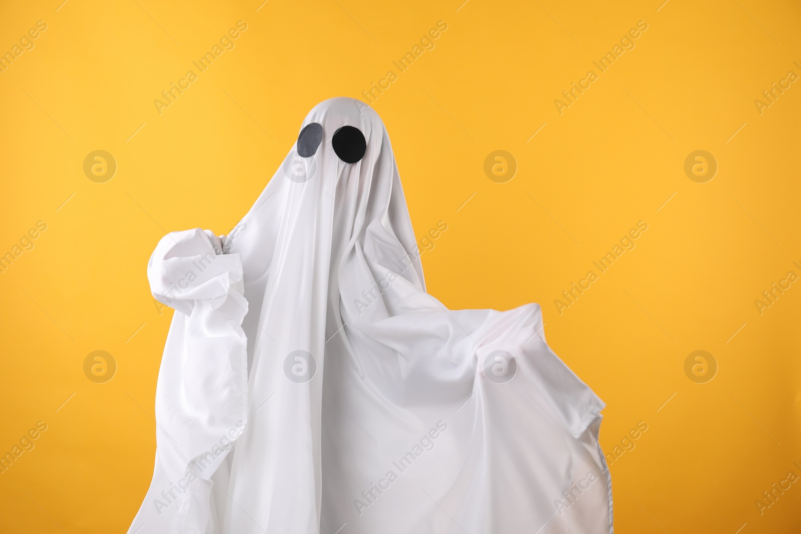 Photo of Creepy ghost. Person covered with white sheet on yellow background, space for text