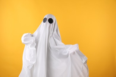 Creepy ghost. Person covered with white sheet on yellow background, space for text