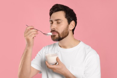Handsome man eating delicious yogurt on pink background