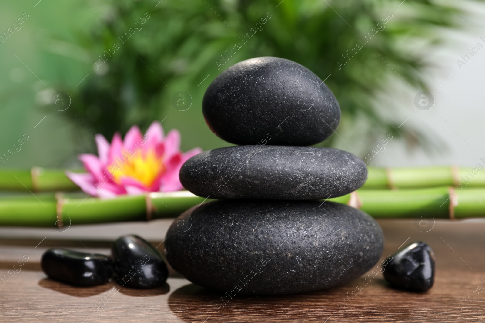 Photo of Stacked spa stones, bamboo stems and flower on wooden table against blurred background