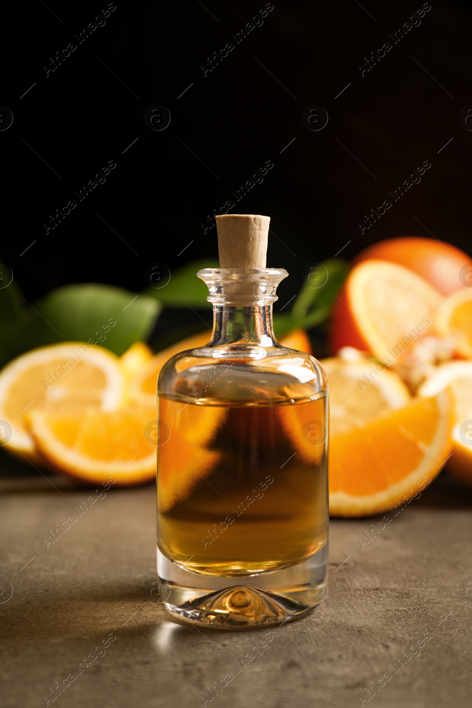 Photo of Bottle of essential oil and citrus fruits on grey table