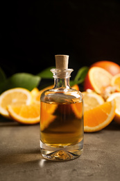 Photo of Bottle of essential oil and citrus fruits on grey table