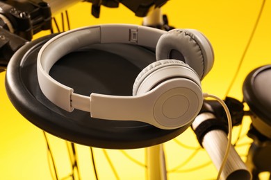 Photo of Modern electronic drum kit with headphones on yellow background, closeup. Musical instrument